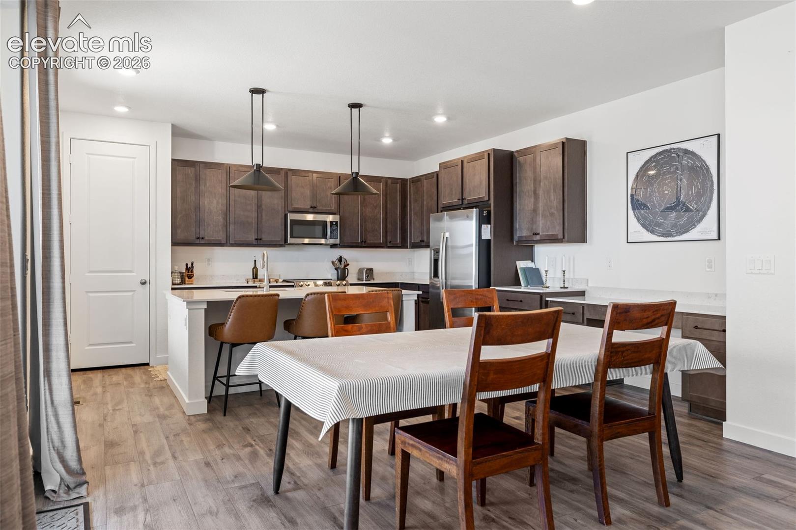 Kitchen featuring dark wood-finish cabinetry, stainless steel appliances, a white countertop island, and pendant lighting