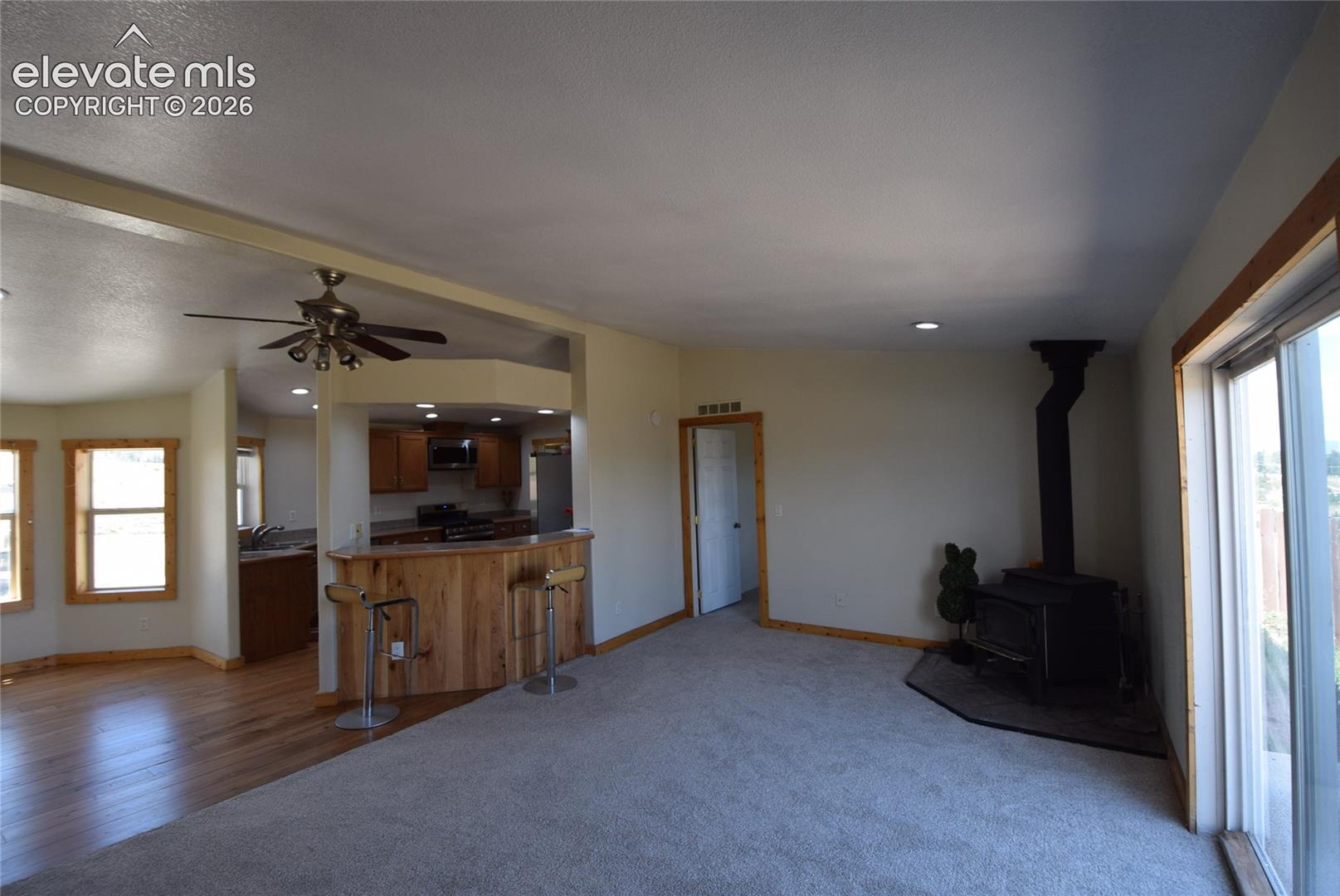 Open-concept living space featuring wood-finish flooring, a wood-burning stove, and a kitchen with wood cabinetry and a breakfast bar