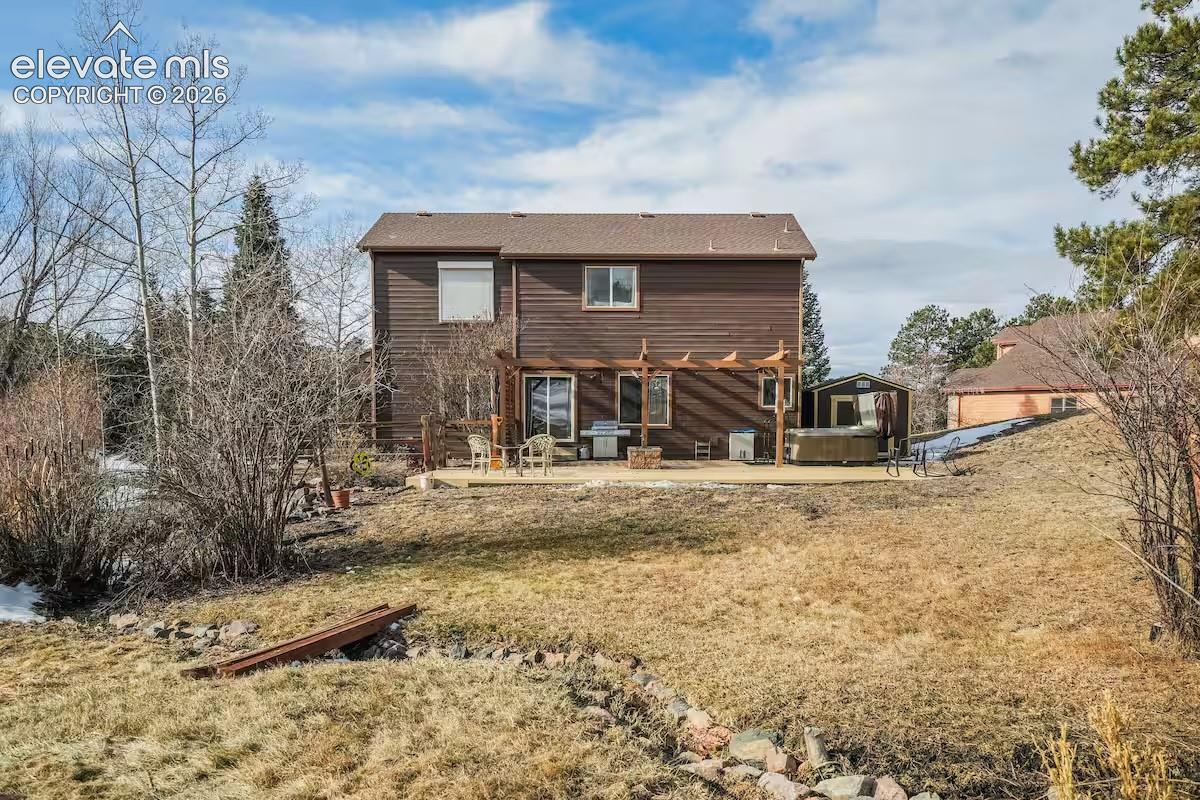 Rear exterior featuring brown siding, a ground-level patio with a wooden pergola, and a built-in outdoor spa