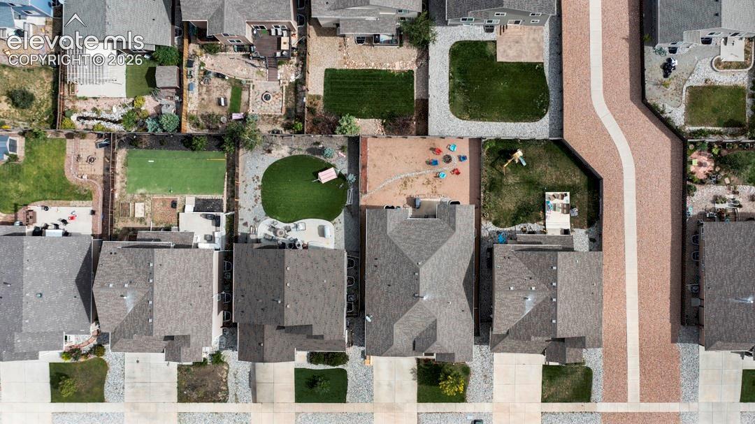 Aerial perspective of a residential property featuring an expansive backyard, a hardscaped patio area, a manicured lawn, and perimeter fencing