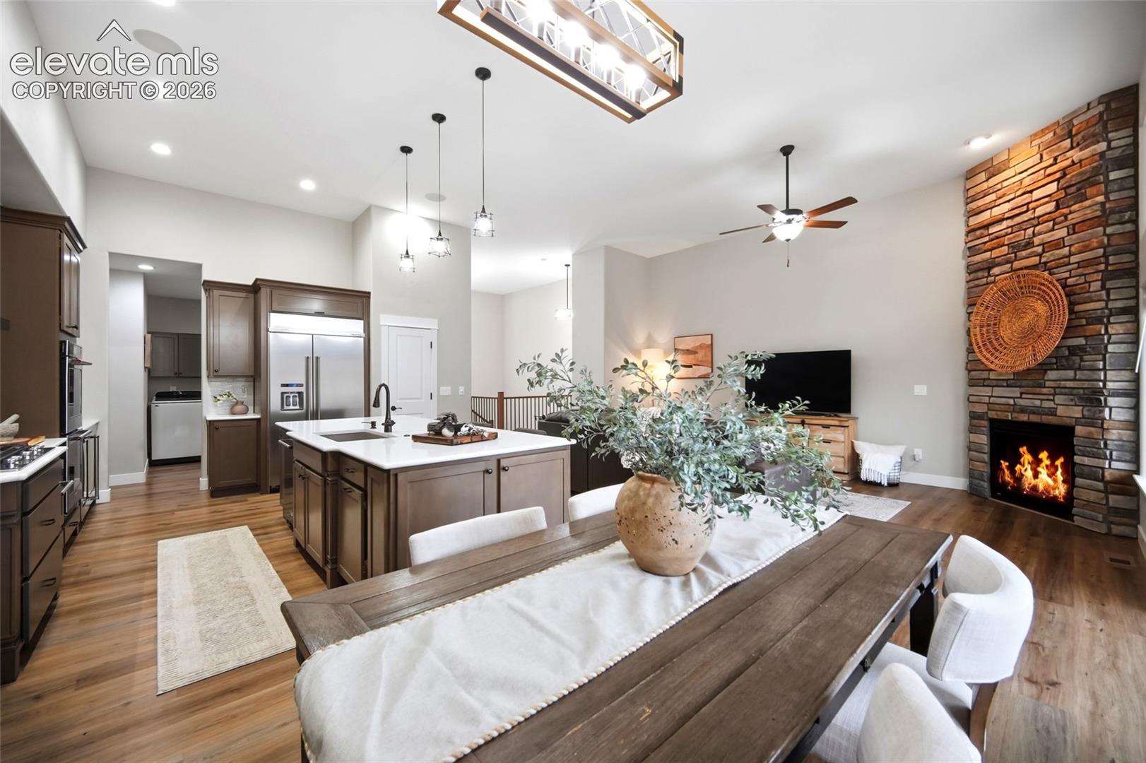 Open-concept living space featuring wood-finish flooring, a kitchen island with quartz countertops, custom cabinetry, a floor-to-ceiling stone fireplace, and varied recessed and pendant lighting