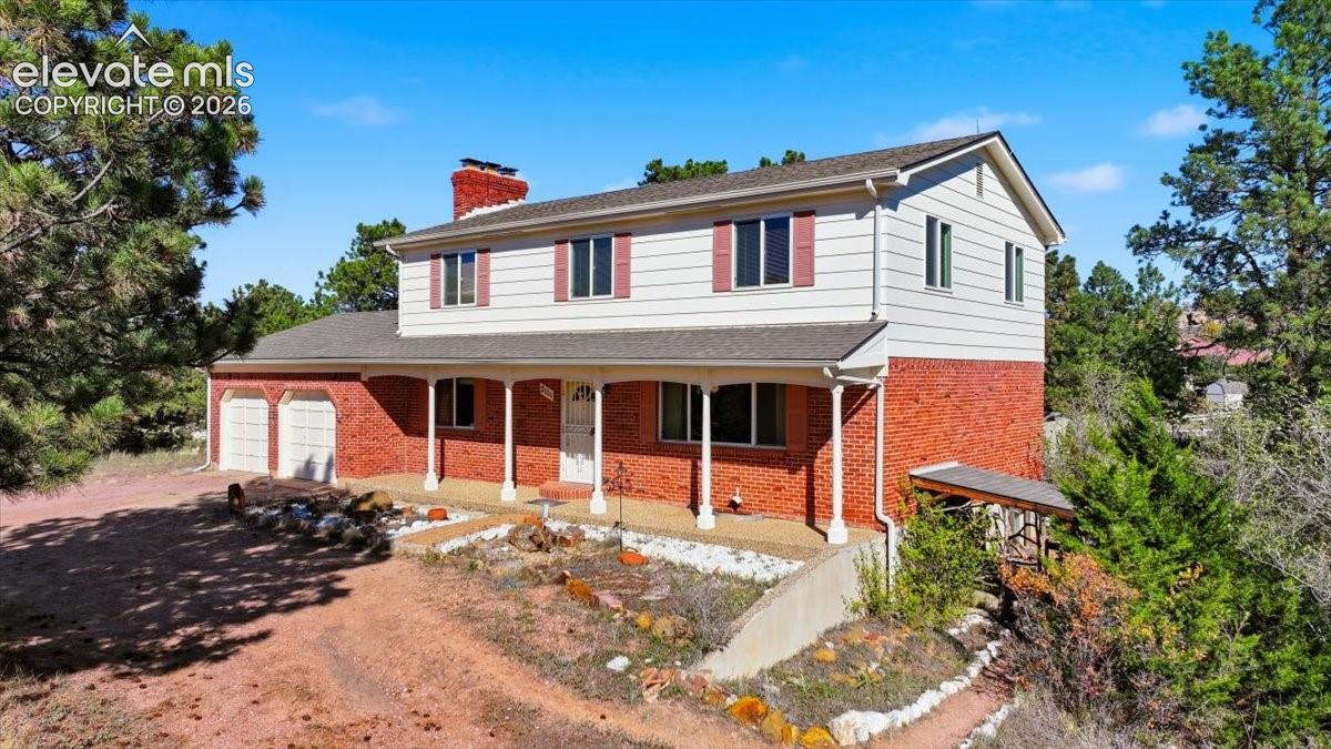 Two-story exterior featuring a brick and horizontal siding facade, covered front porch with support columns, attached two-car garage, and a brick chimney