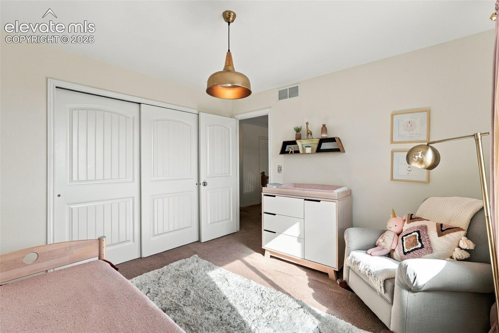 Interior room featuring neutral wall paint, white multi-panel closet doors, and a metallic pendant light fixture