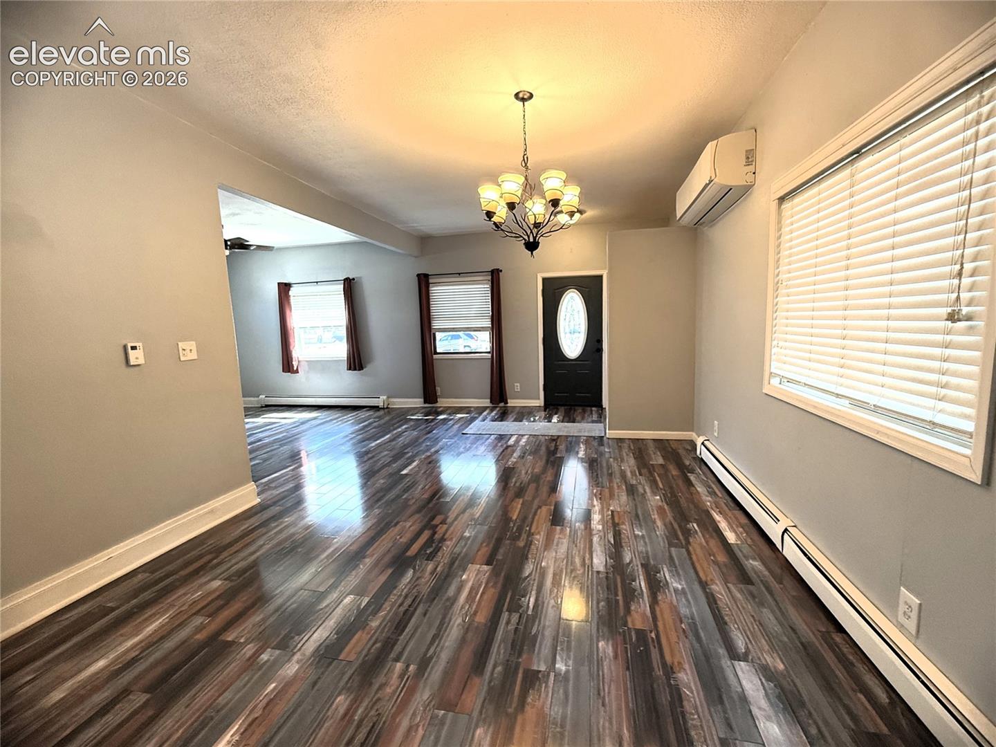 Wood-finish flooring, wall-mounted ductless mini-split system, multi-light chandelier, and front entrance door featuring an oval glass insert