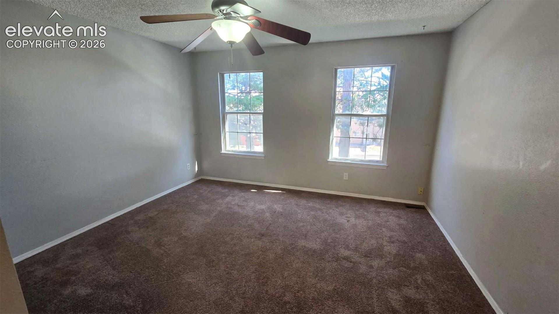 Neutral wall tones, wall-to-wall carpeting, two double-hung windows, and a ceiling fan with integrated lighting