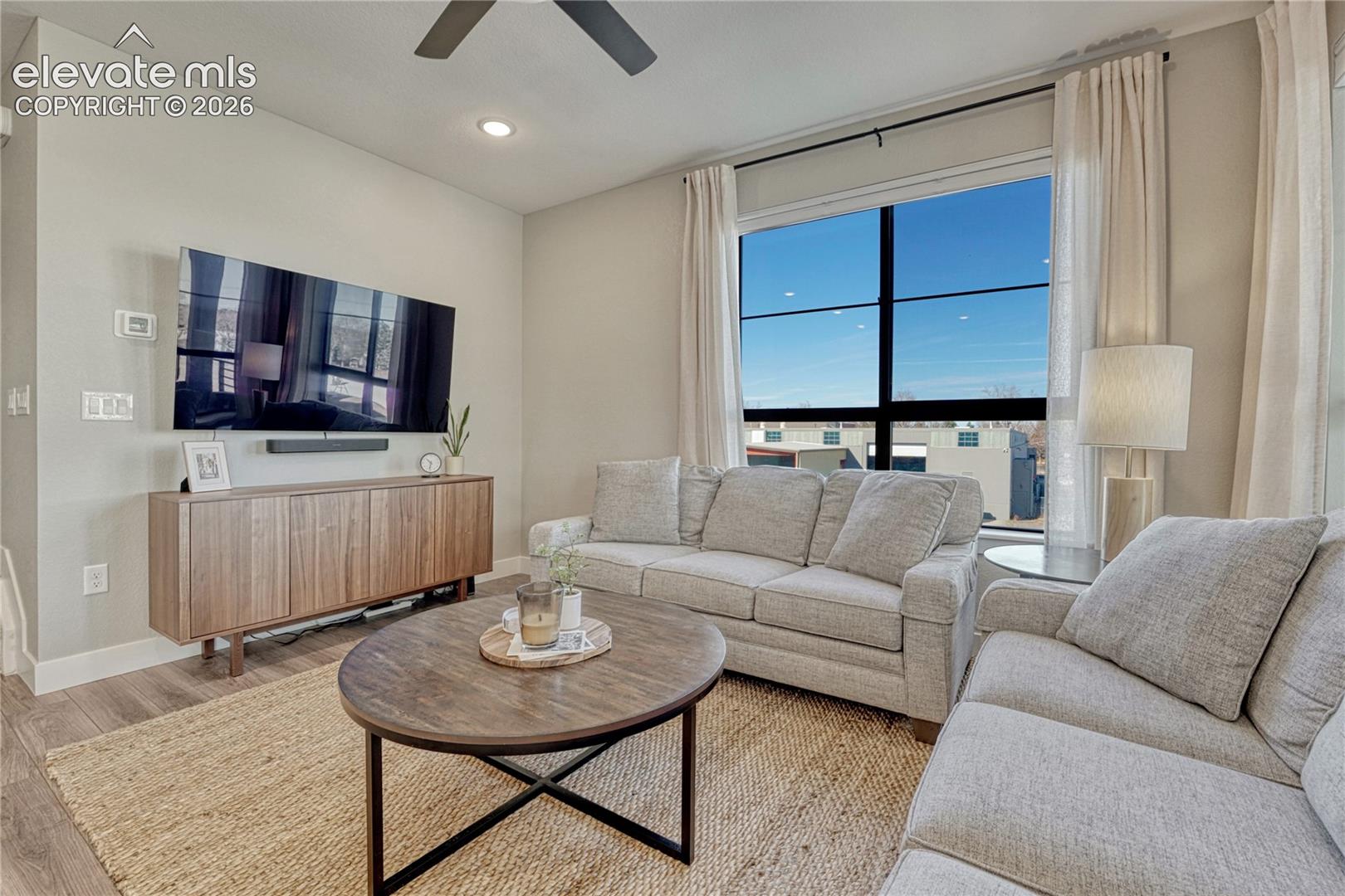 Living area featuring high ceilings, wood-finish flooring, recessed lighting, a ceiling fan, and a large multi-pane window