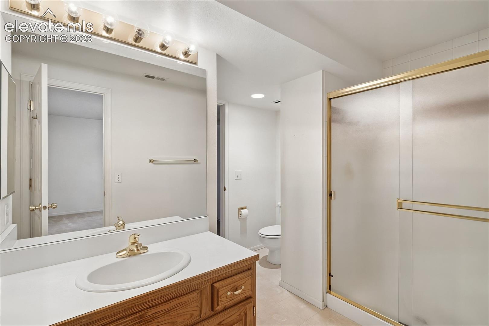 Bathroom featuring a vanity with a white countertop and oval sink, wall-spanning mirror, multi-bulb vanity light, and a shower with a sliding glass door