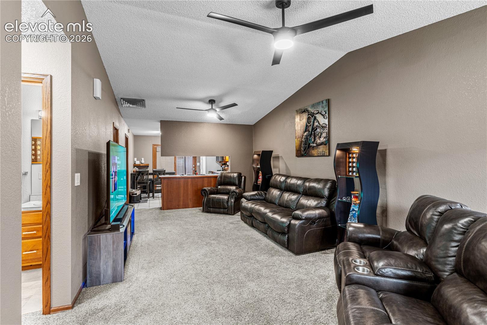 Vaulted ceilings with dual matte black ceiling fans, neutral carpeting, and a built-in wooden half-wall partition