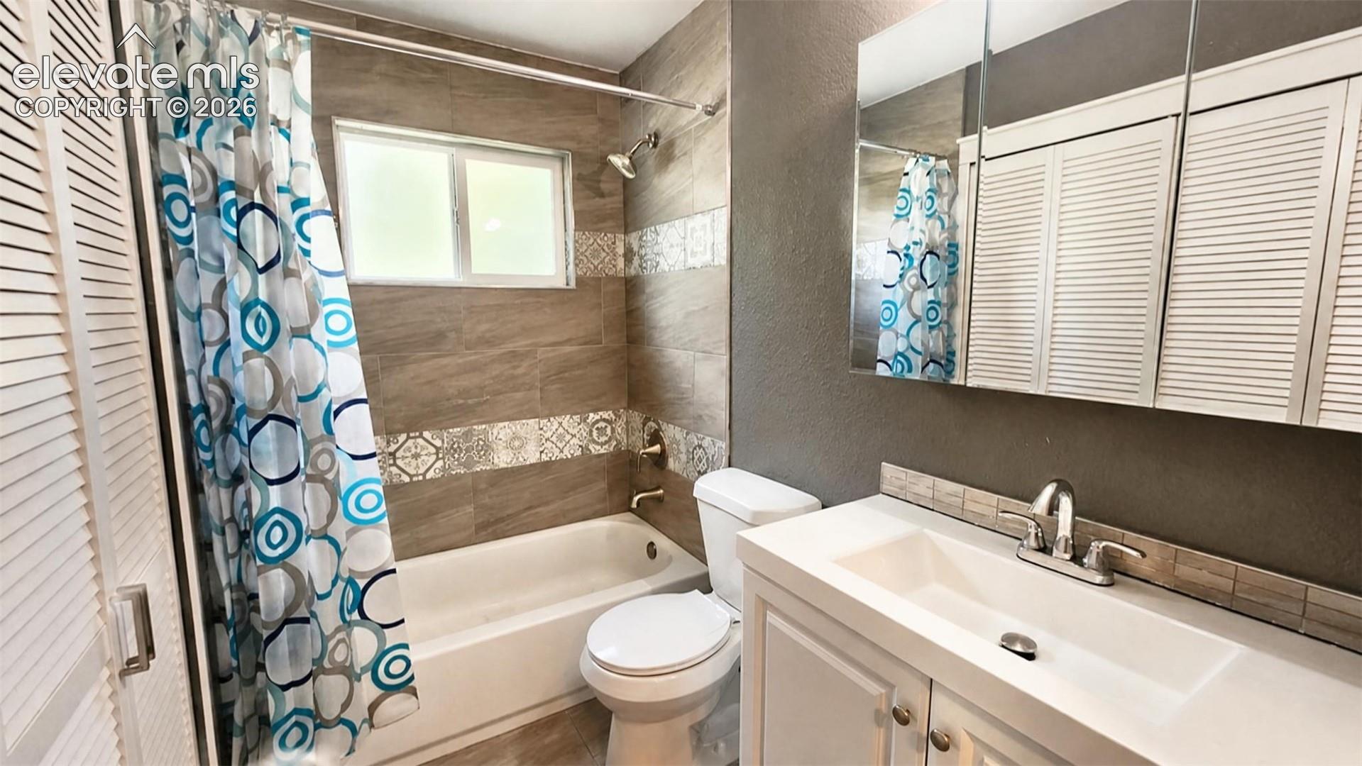 Bathtub with surrounding tile, single window, upgraded sink, chrome-finish faucet, and mirrored medicine cabinet