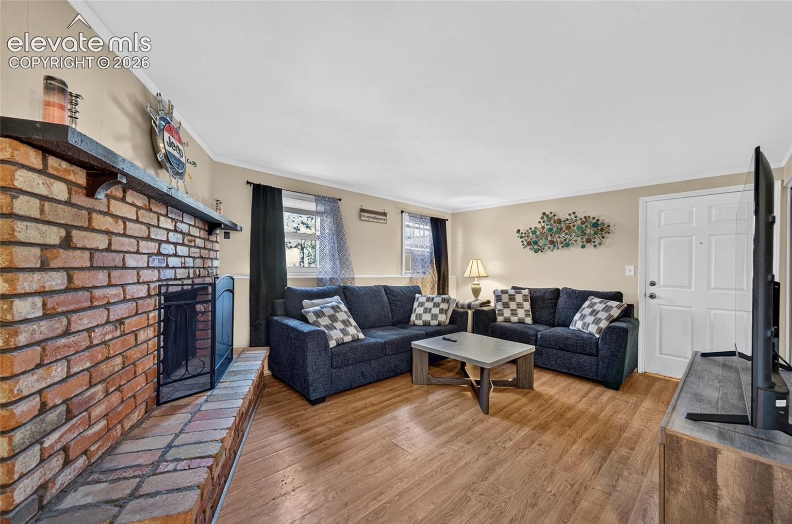 Living area featuring wood-finish flooring, a floor-to-ceiling brick fireplace with a custom mantle, and an exterior entry door