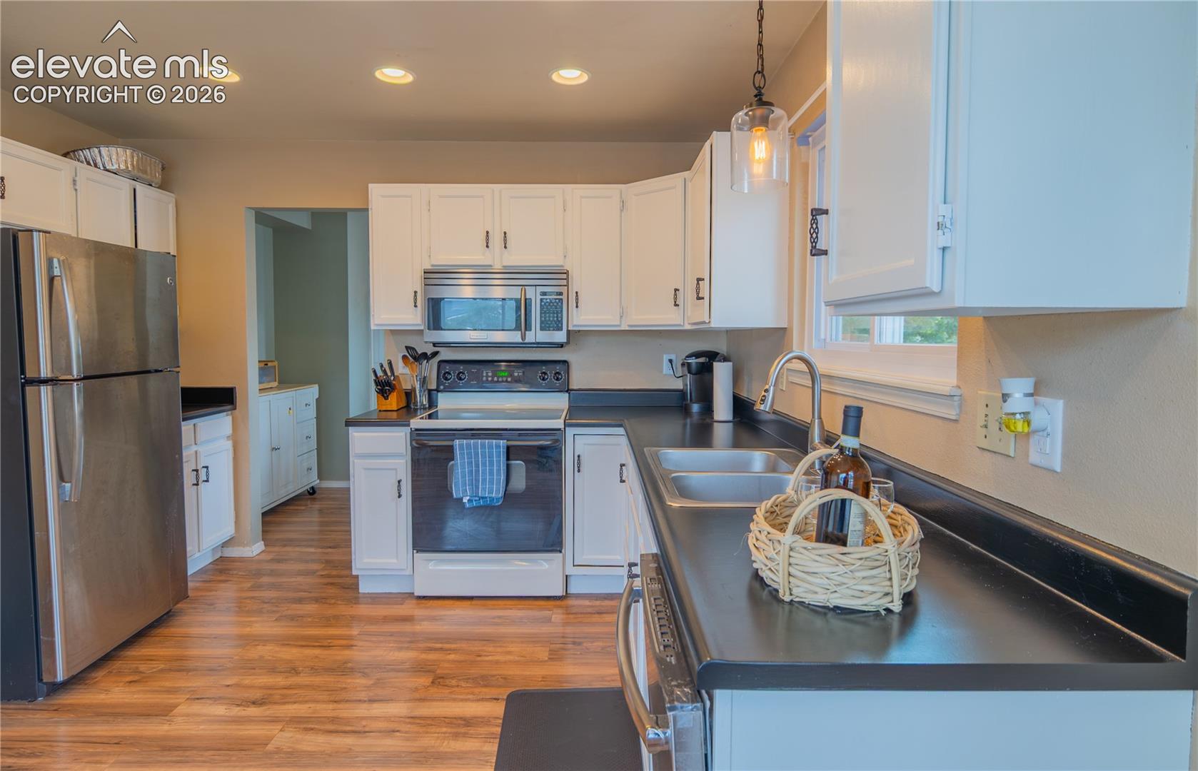 Kitchen featuring white cabinetry, wood-finish flooring, stainless steel appliances, black countertops, and recessed lighting