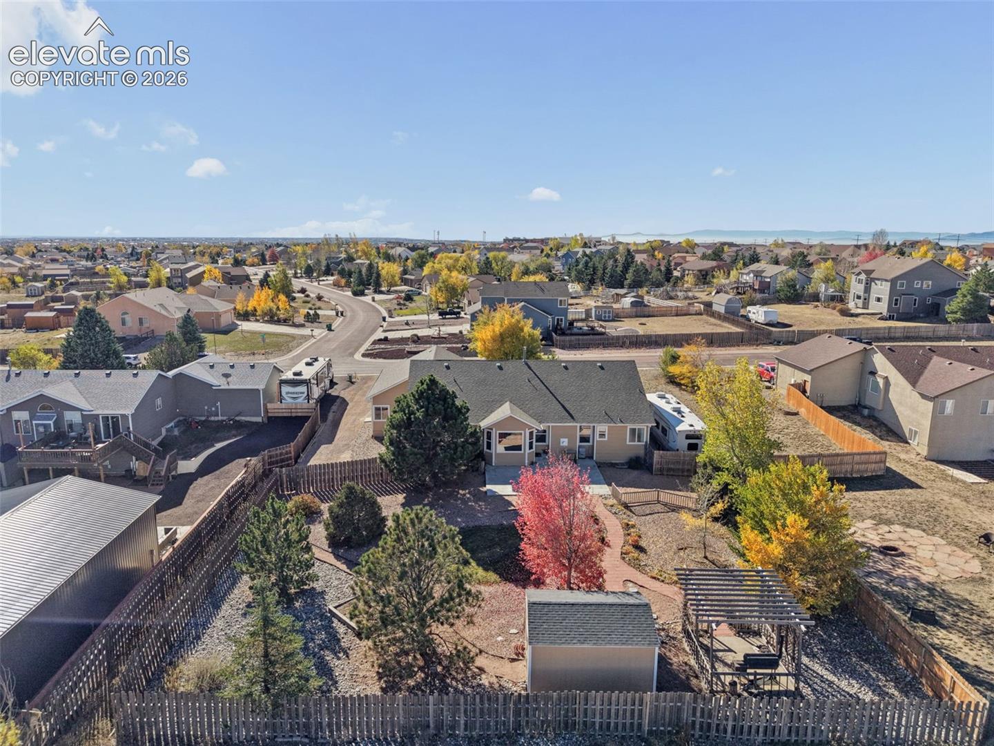 Aerial perspective of a property featuring a fenced backyard, an attached pergola, a detached storage shed, and a paved walkway