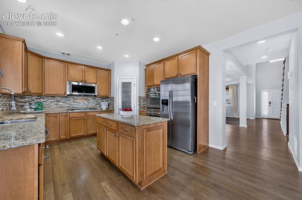 Kitchen with wood-finish flooring, granite countertops, an island, and stainless steel appliances, including a built-in microwave and oven