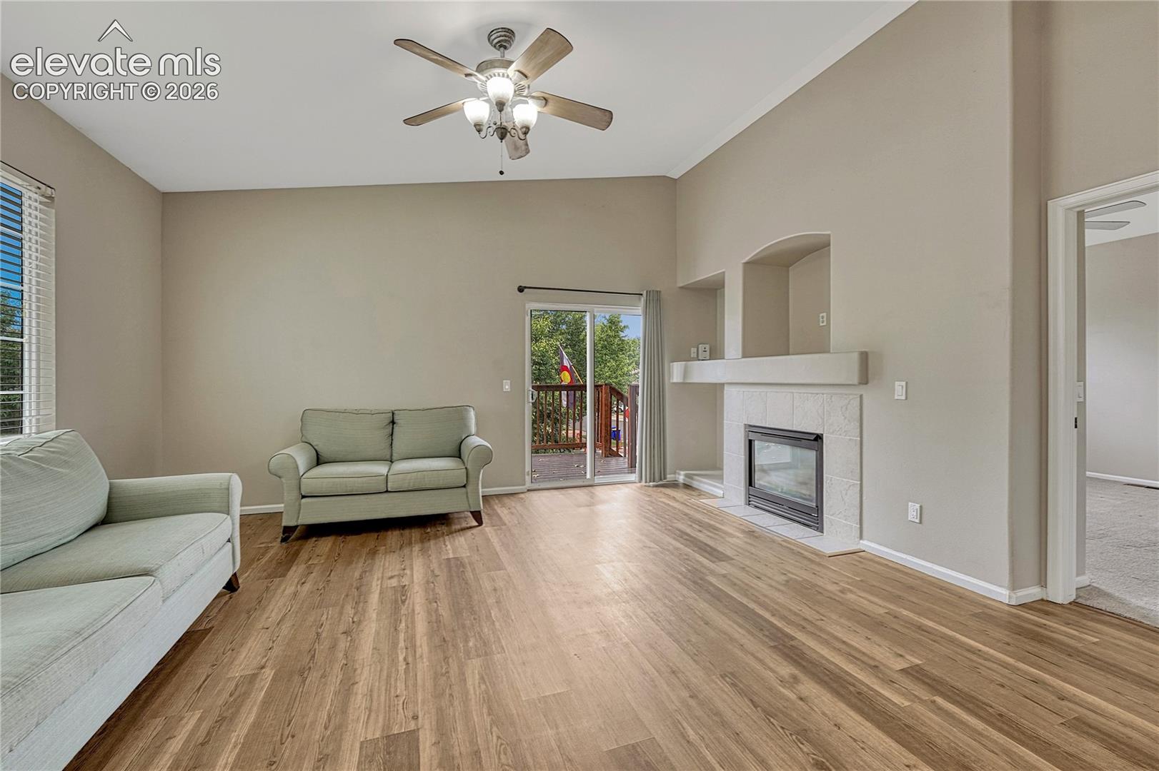 Vaulted ceilings, wood-finish flooring, fireplace with a tiled surround, recessed wall niche, and sliding glass door