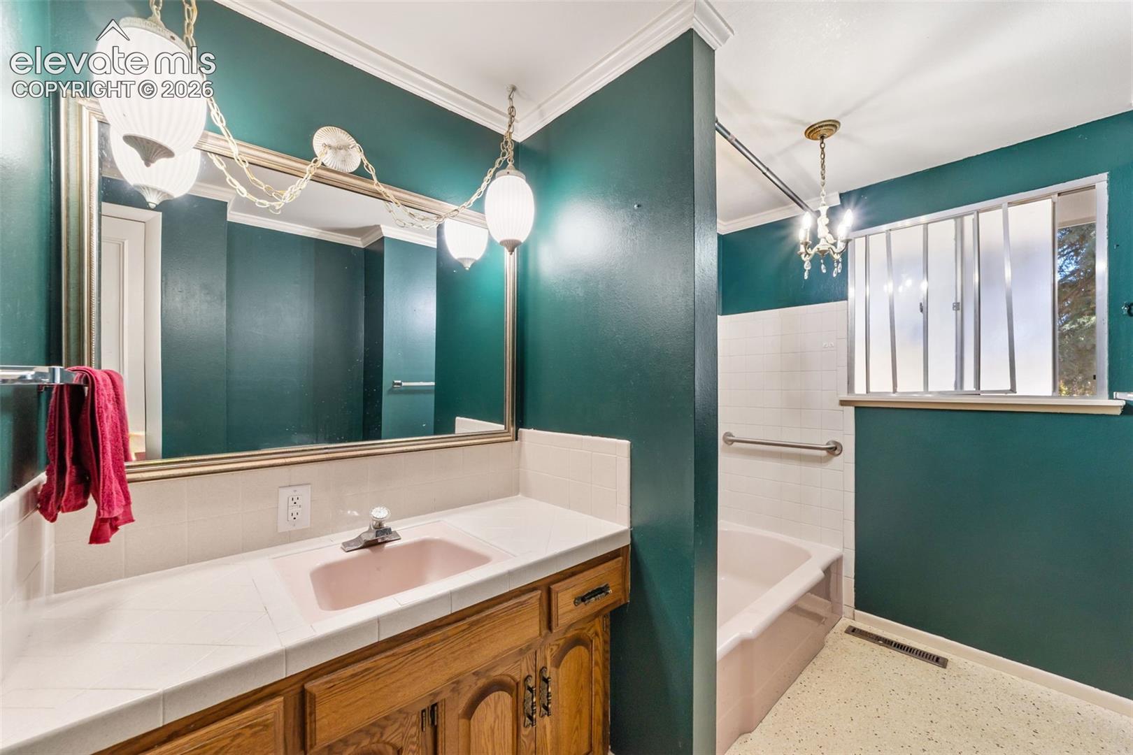 Bathroom vanity featuring a tile countertop with a pink drop-in sink, wood-finish cabinetry, and an expansive wall mirror