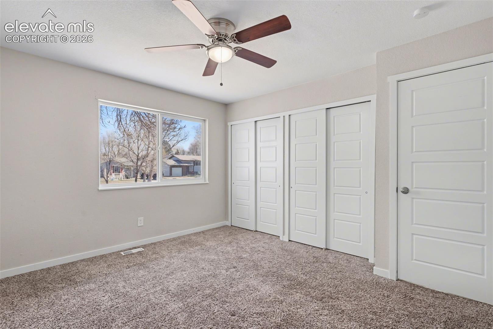 Room featuring neutral-toned carpeting, dual sliding closet doors with raised panels, a five-panel interior door, and a ceiling fan with integrated lighting