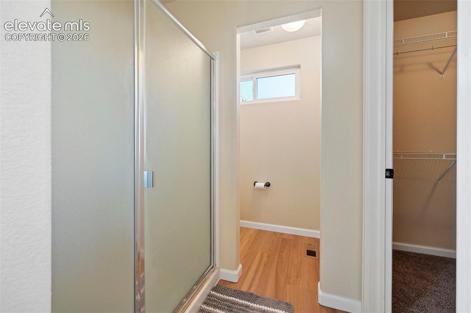 Bathroom featuring a shower stall with a framed glass door, wood-finish flooring, and a walk-in closet with wire shelving
