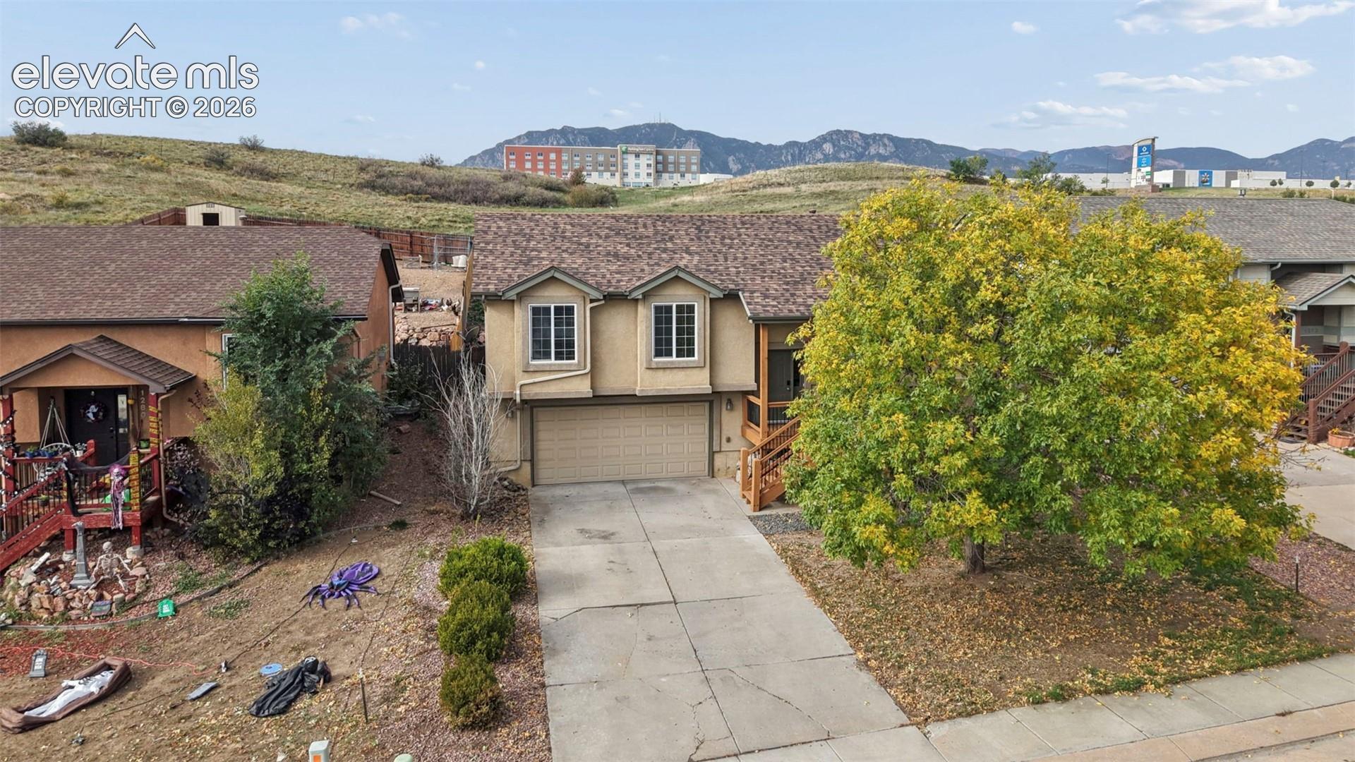 Stucco exterior featuring a concrete driveway, two-car garage, shingle roof, and mountain backdrop