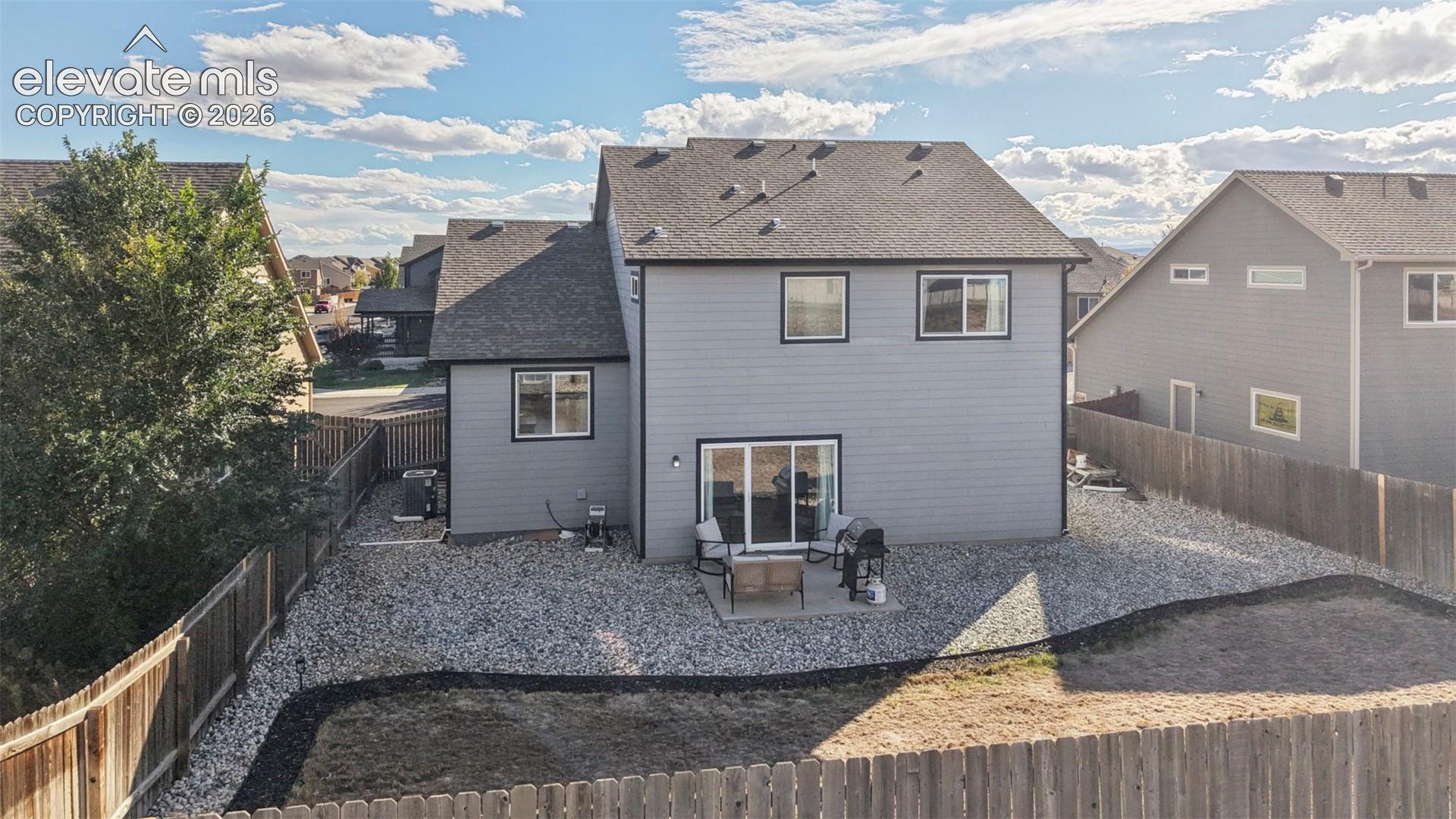Two-story exterior featuring gray lap siding, a concrete rear patio, rock-landscaped yard, and privacy wood fencing