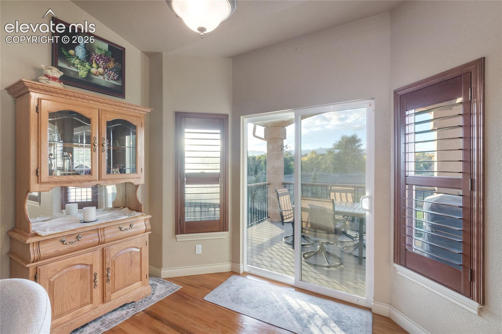 Sliding glass door to the covered deck, wood-finish flooring, and wooden shutters