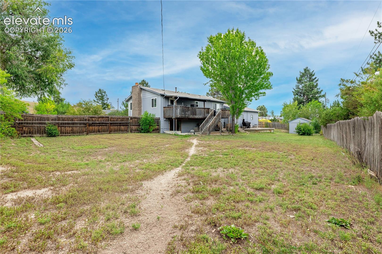 Expansive backyard featuring wood perimeter fencing, mature trees, a raised exterior deck, and a detached storage structure