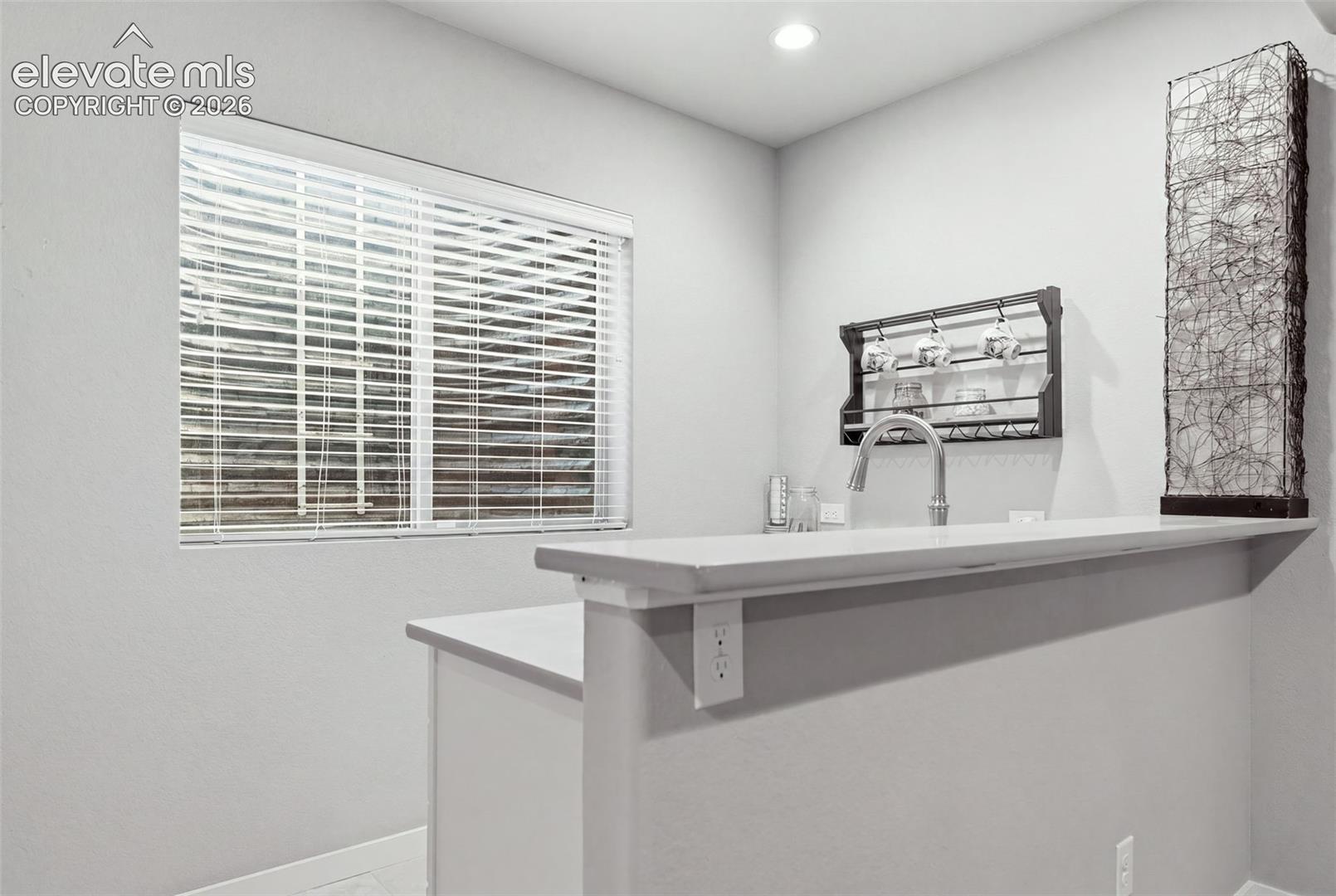 Built-in counter with a stainless steel faucet, wall-mounted cup rack, and recessed lighting.