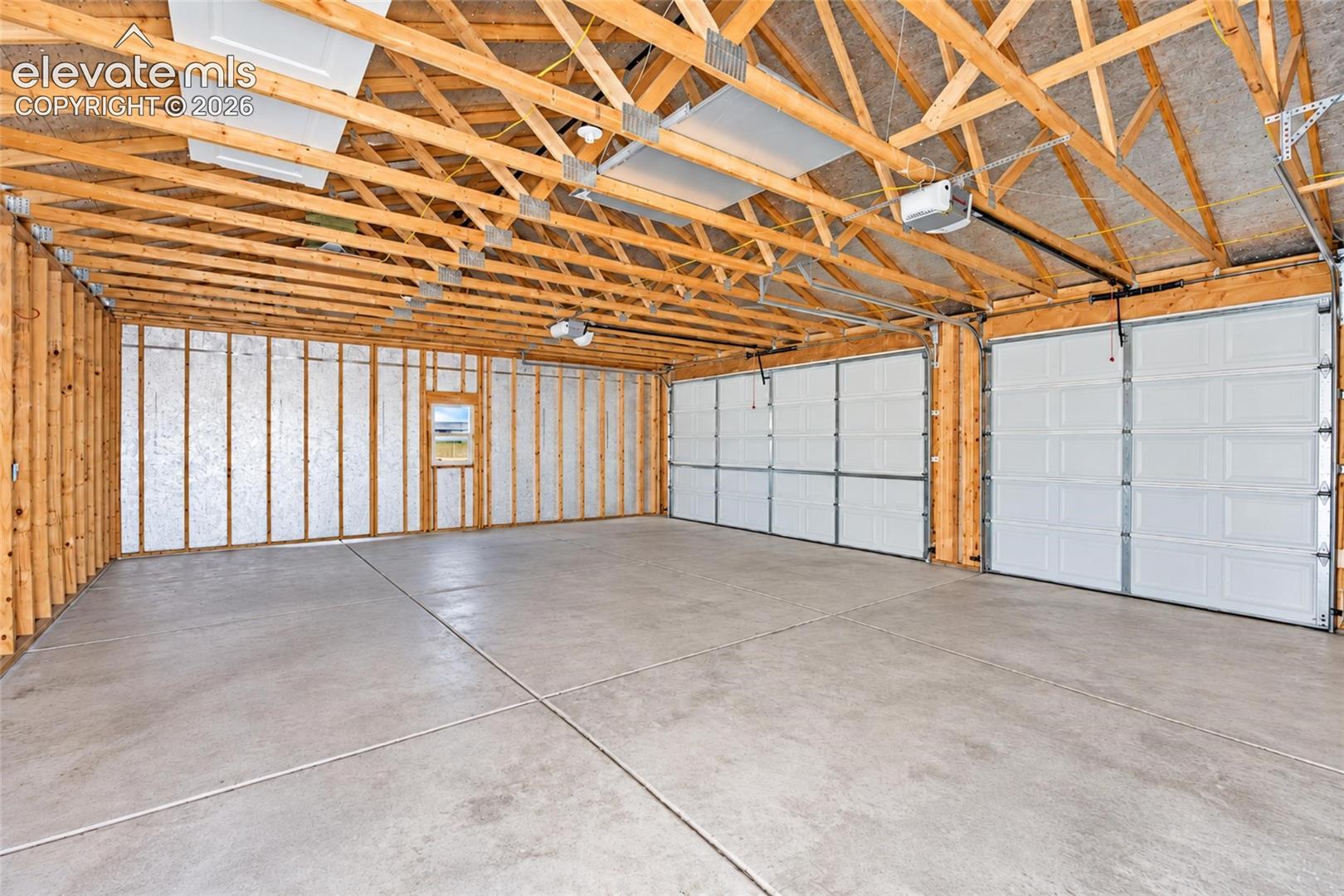Expansive three-bay garage featuring exposed wood truss framing, concrete flooring, reflective interior wall insulation, and three automated metal roll-up doors