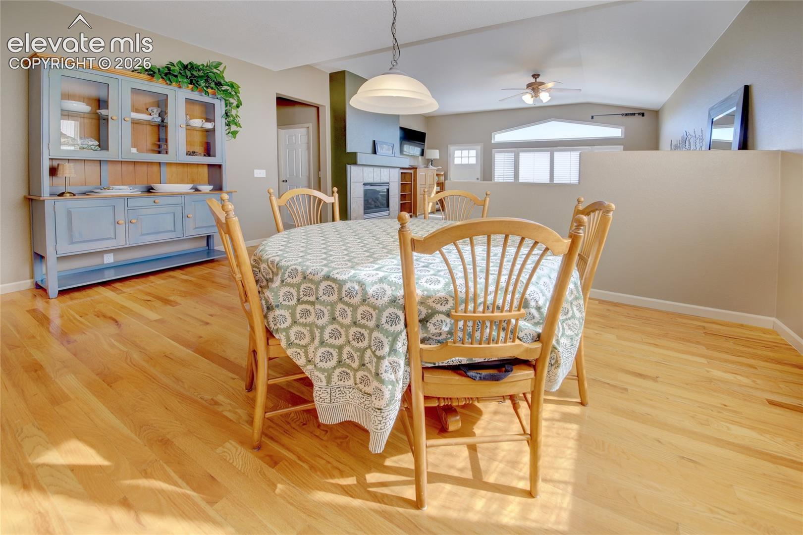 Dining area featuring wood-finish flooring, a built-in hutch, a fireplace with a mantel, a pendant light fixture, and vaulted ceilings