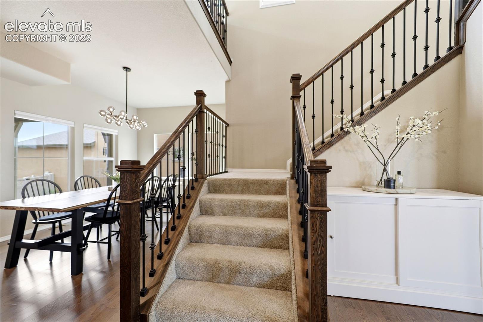 Wood-finish flooring, carpeted staircase with wrought iron balusters, built-in white cabinetry, and a modern chandelier