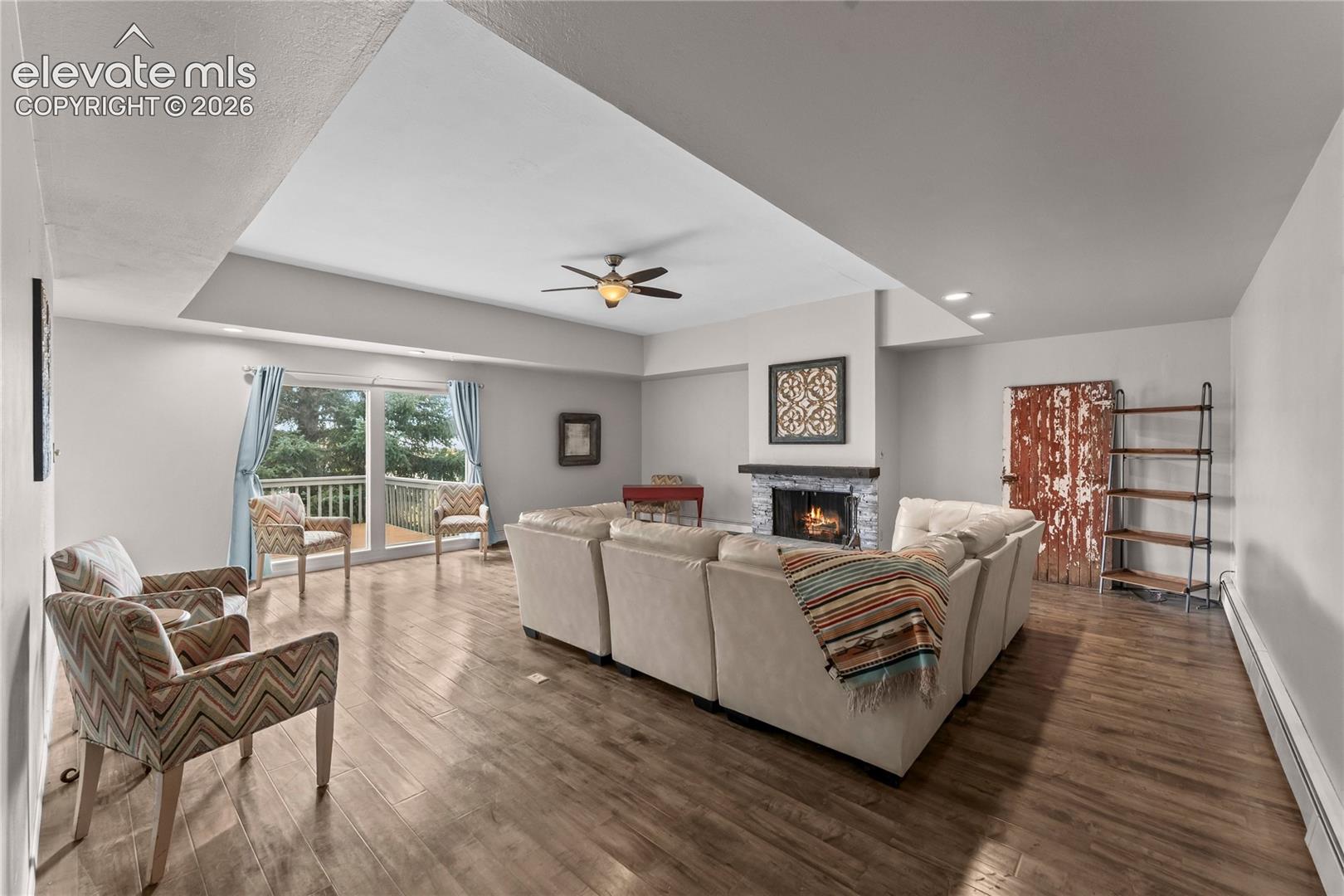 Tray ceiling, wood-finish flooring, fireplace with stone surround, recessed lighting, and sliding glass doors