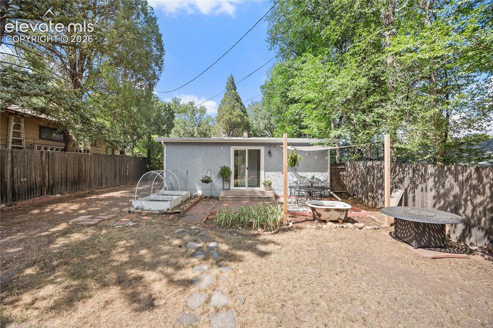 Rear exterior featuring a sliding glass door, a brick patio area, a privacy fence, and a raised garden bed