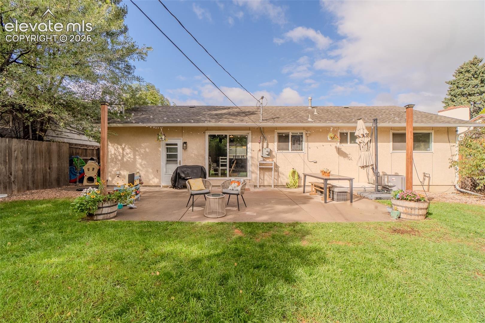 Rear exterior featuring a concrete patio, wood fence perimeter, sliding glass door, and mature trees