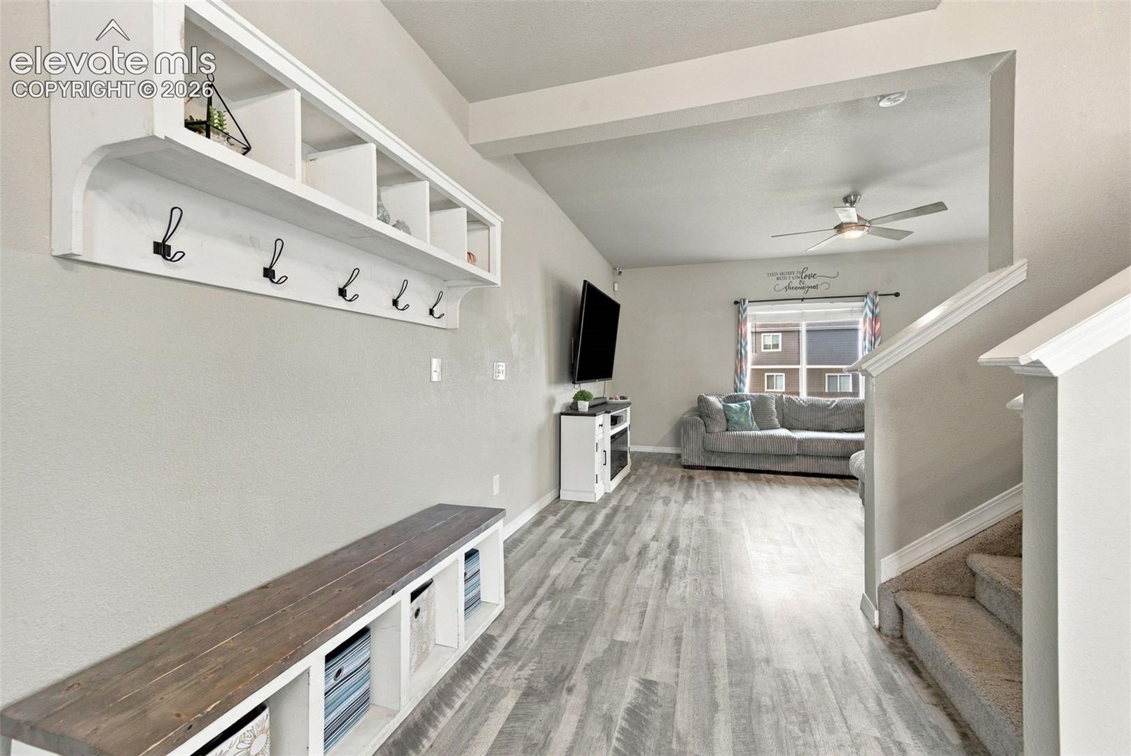 Built-in wall-mounted coat rack with shelving, wood-top bench with integrated cubbies, wood-finish flooring, and ceiling fan