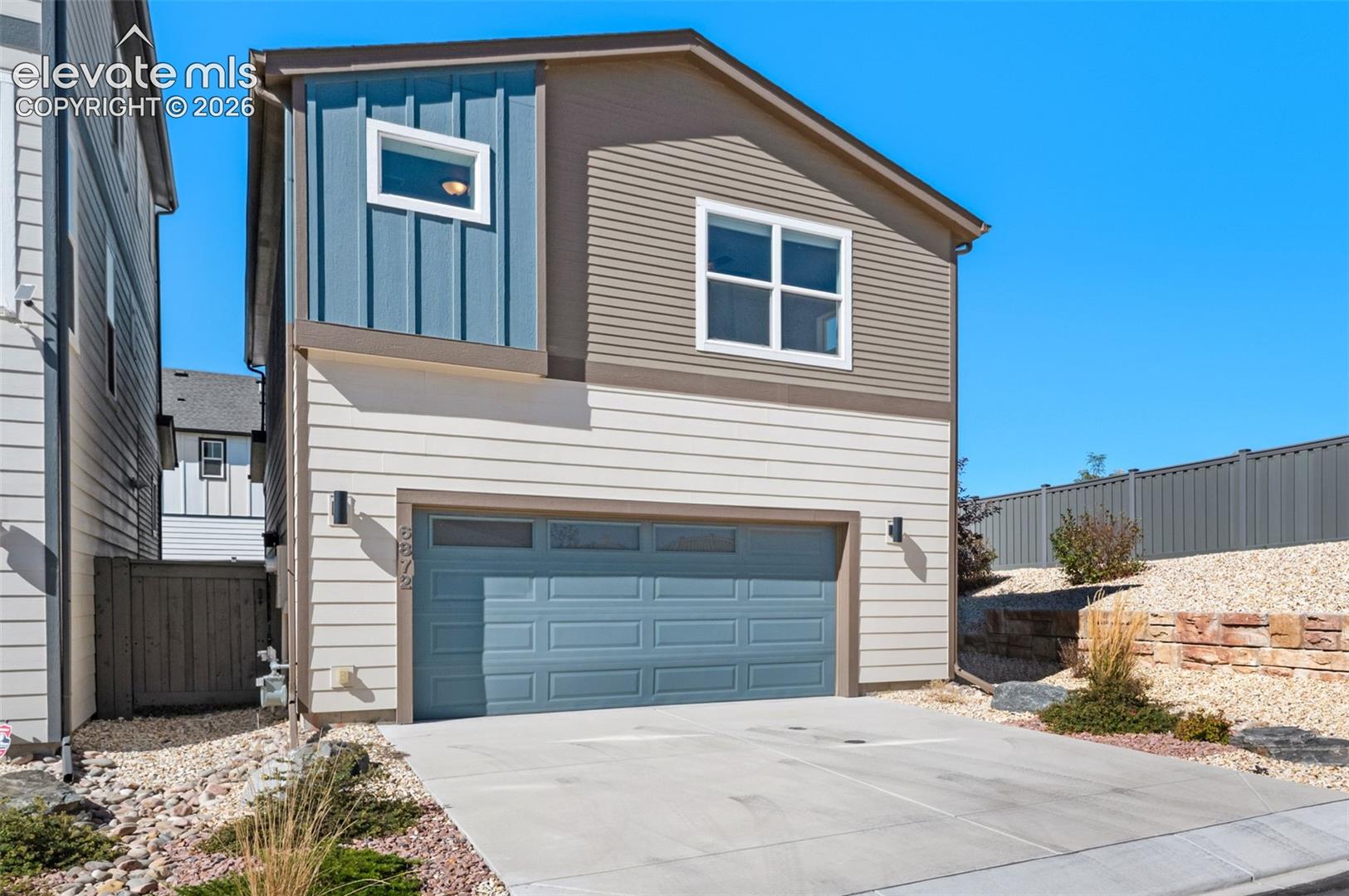 Multi-level exterior featuring horizontal and vertical lap siding, an attached two-car garage with a rectangular window panel, and decorative stacked-stone retaining walls