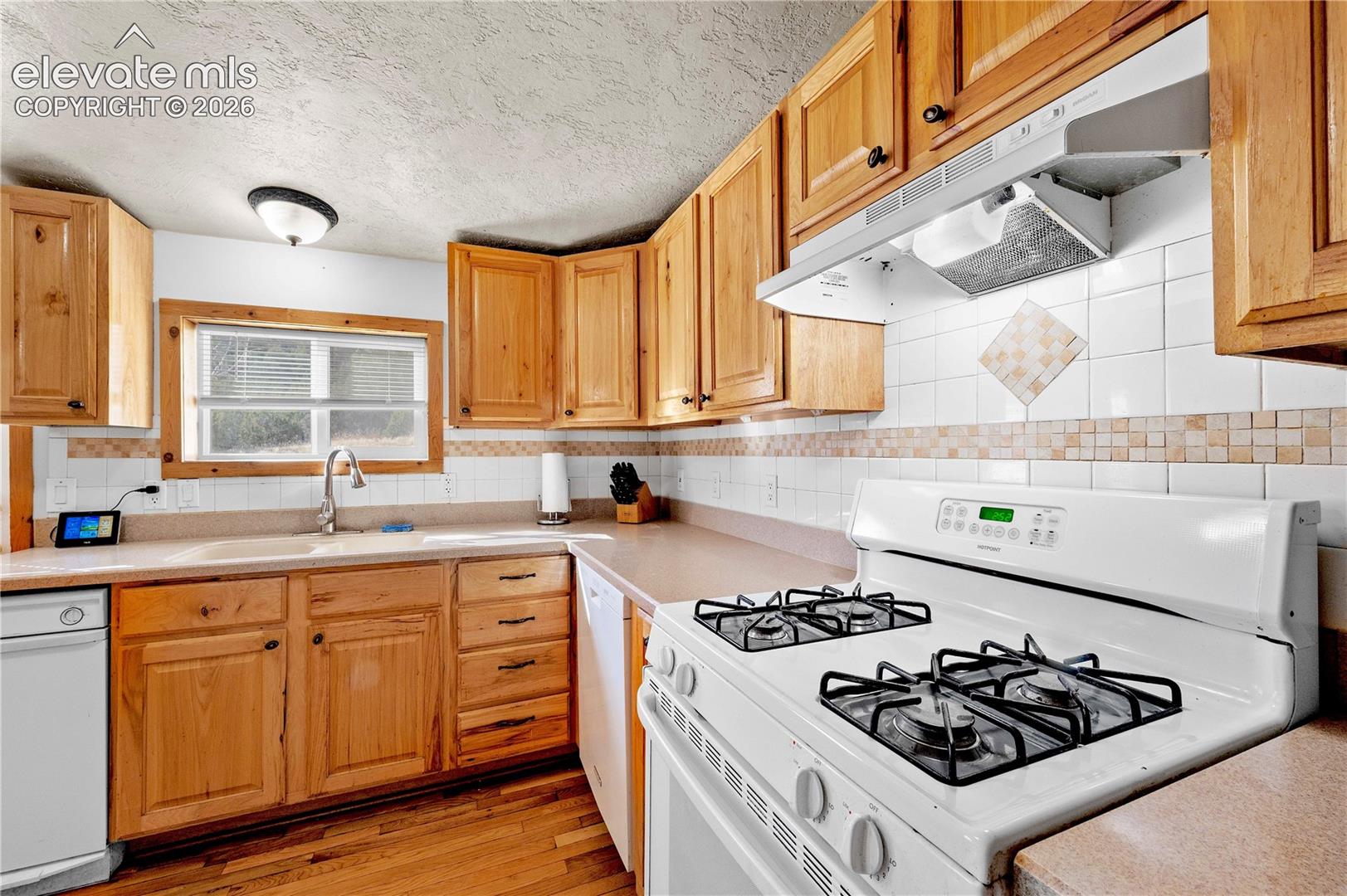 Kitchen featuring backsplash, sink, light wood-type flooring, a textured ceiling, and white appliances