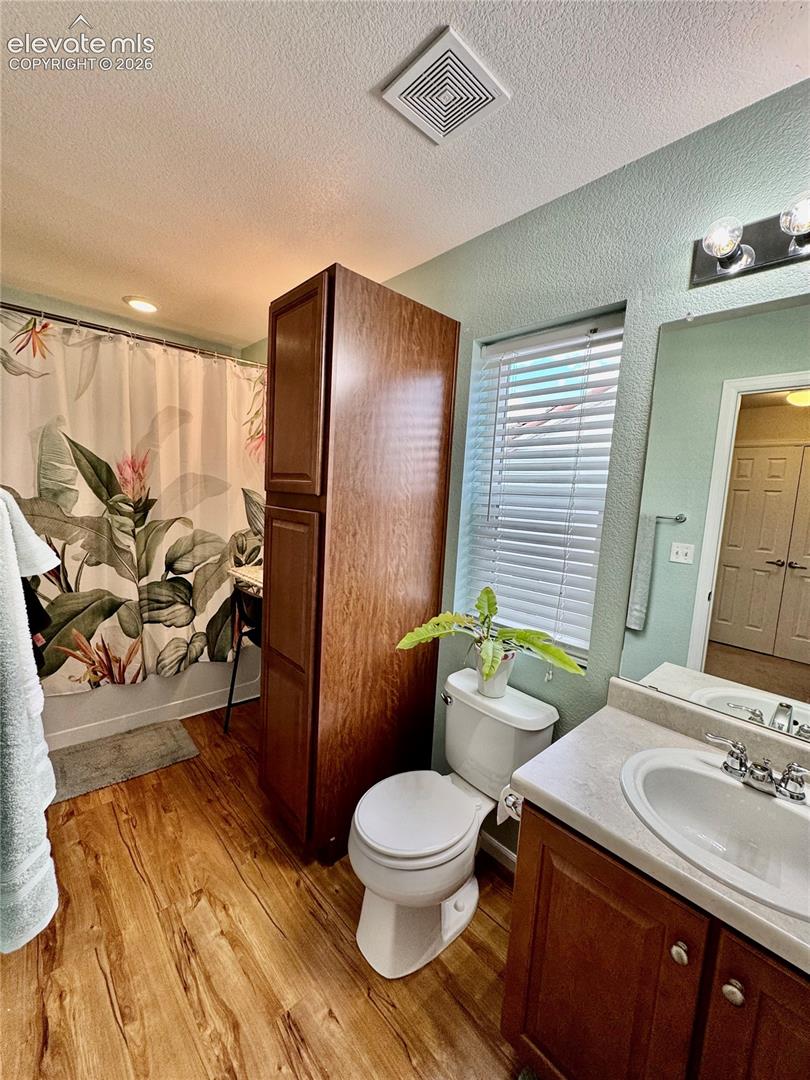 Bathroom featuring wood-finish flooring, a vanity with a white basin sink, and a built-in wood-finish storage cabinet