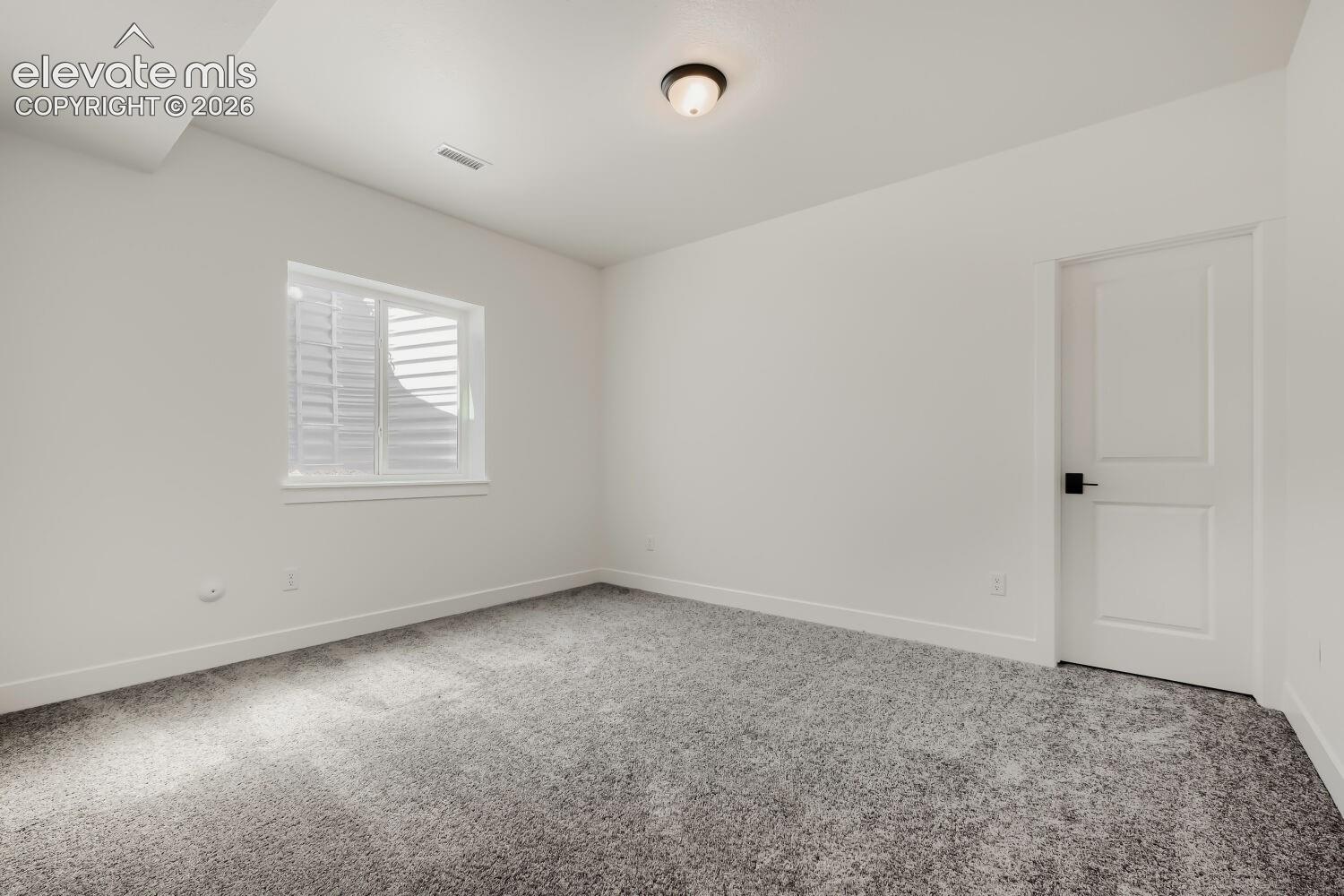 Room with neutral carpeting, white interior paint, and a window featuring white plantation shutters