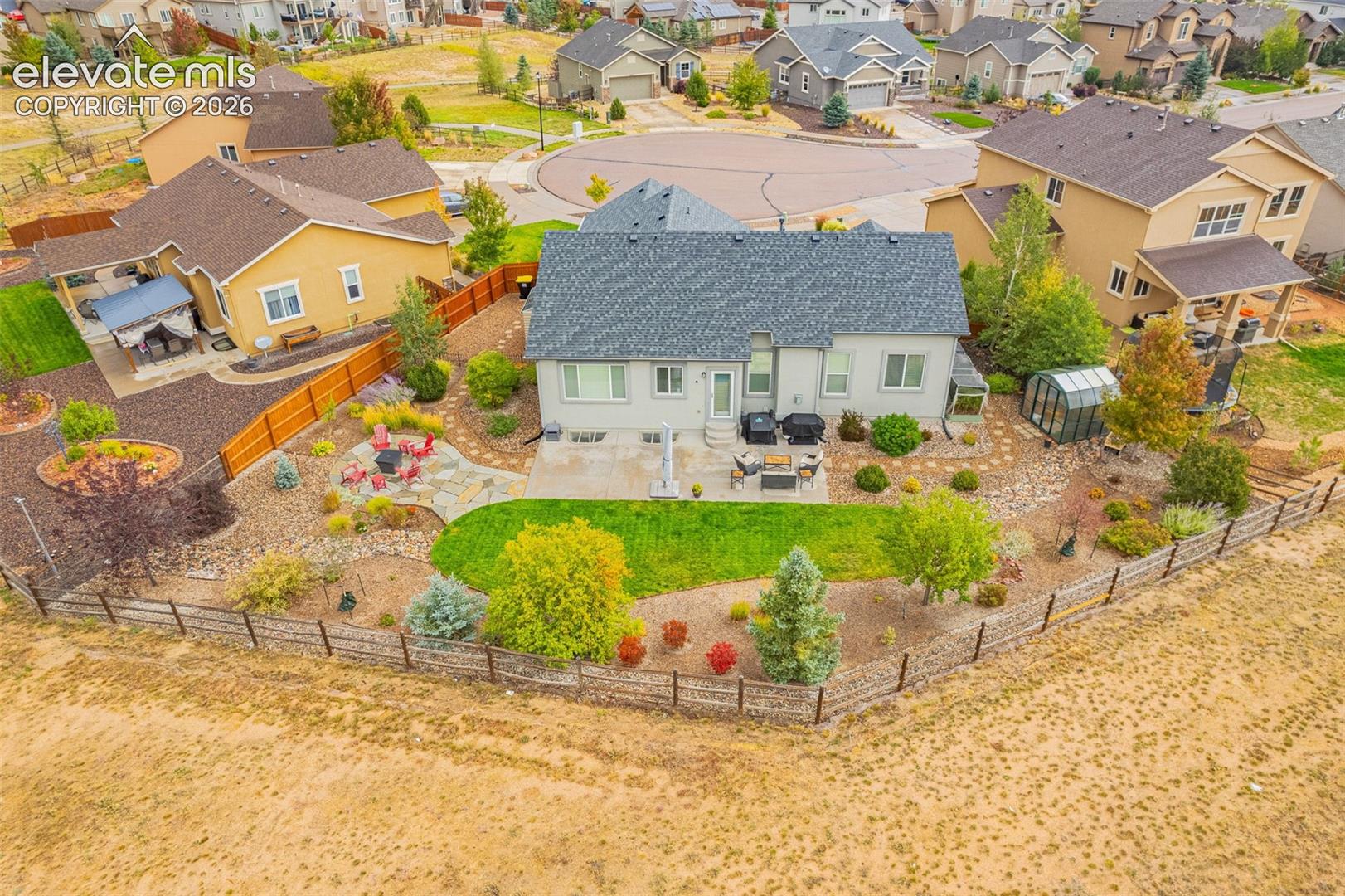Landscaped backyard featuring a stone patio, concrete terrace, manicured lawn, and a perimeter split-rail fence