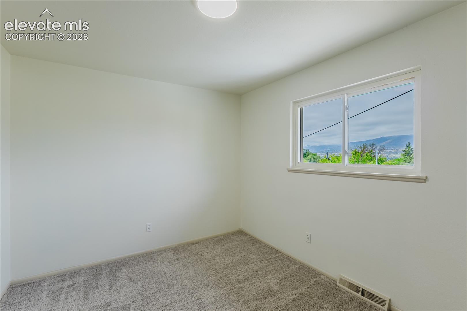  2nd Bedroom - Light-filled room featuring a broad window, white painted walls, and gray carpet flooring