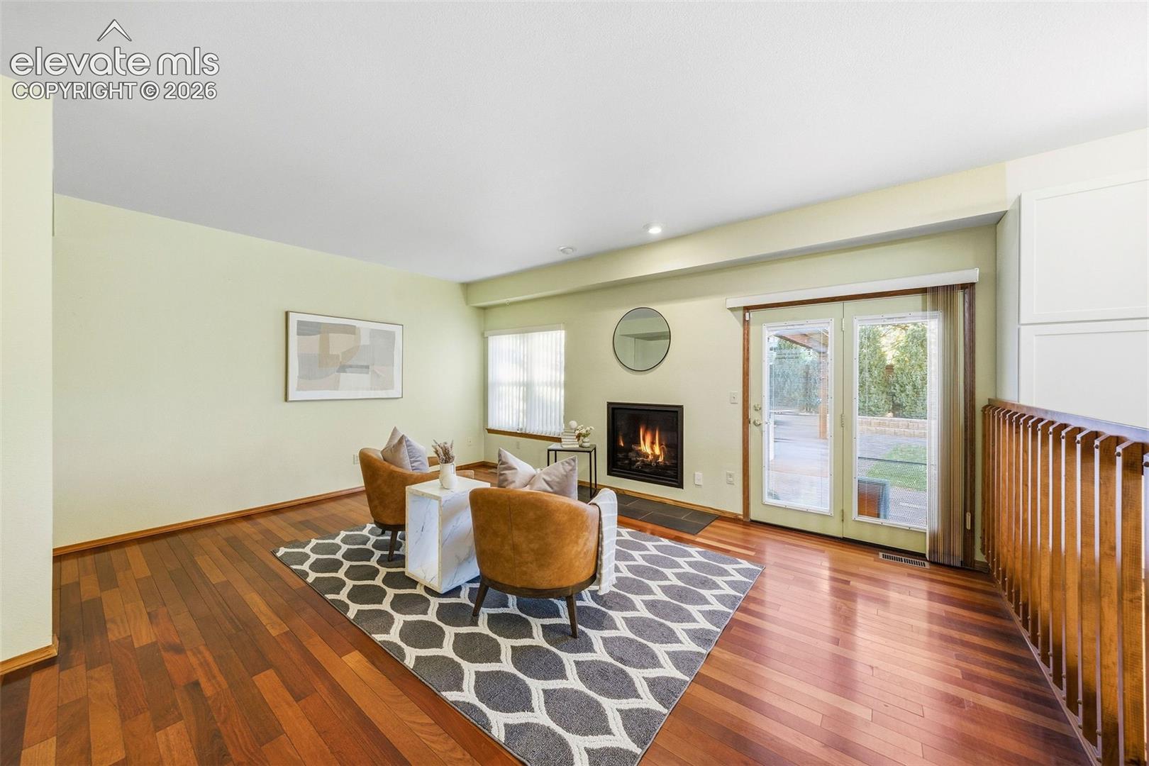 Wood-finish flooring, fireplace with a black surround, and double glass-paneled exterior doors with integrated sidelights, complemented by a vertical slat wood-finish railing