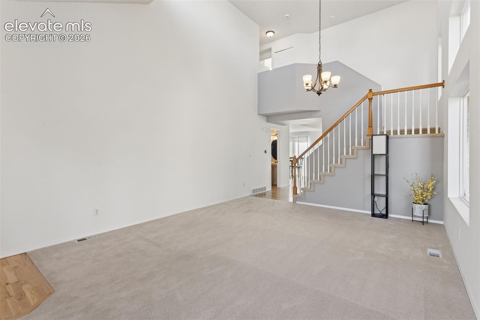 Dining room next to formal living room with vaulted ceilings,  decorative chandelier, and expansive windows