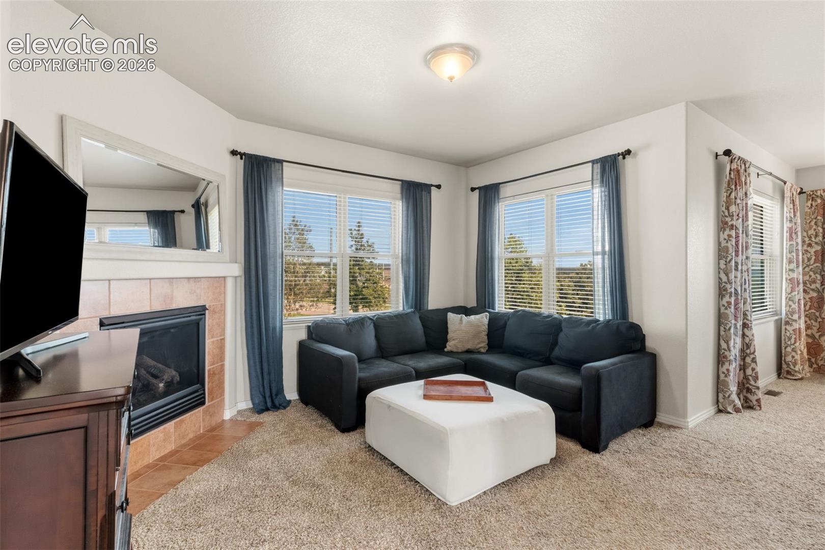 Large sitting area with carpeted area featuring a corner window arrangement, a tiled fireplace with a mantel, and a flush-mount ceiling light fixture