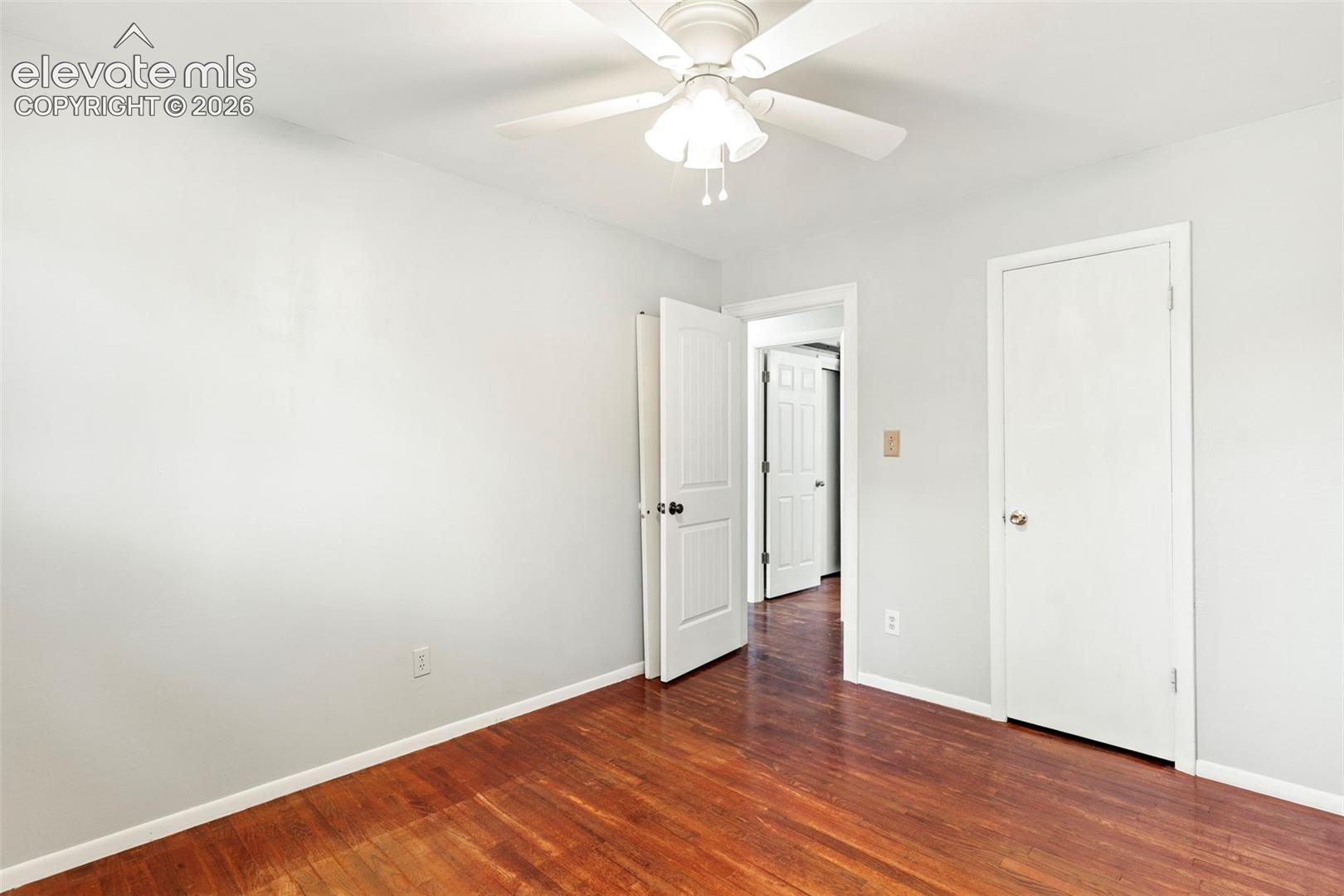 Hardwood flooring, light gray wall paint, white trim, white doors, and a ceiling fan with integrated lighting