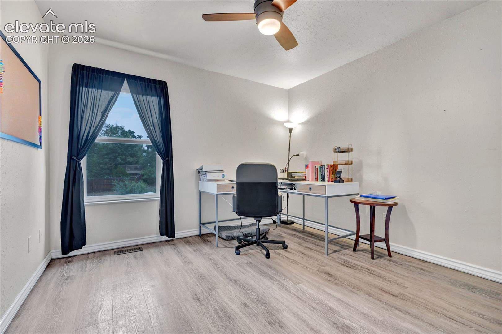 Spacious room featuring wood-finish flooring, a ceiling fan with integrated lighting, and a window with trim molding