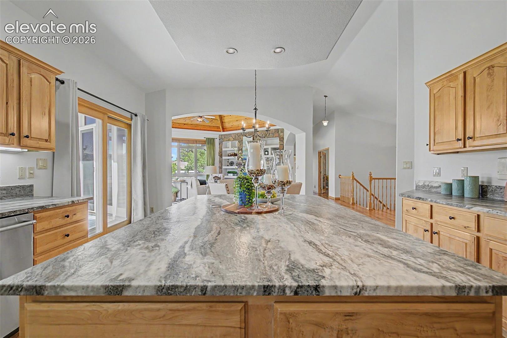 Spacious kitchen island with a patterned countertop, recessed lighting, wood cabinetry, and stainless steel appliances
