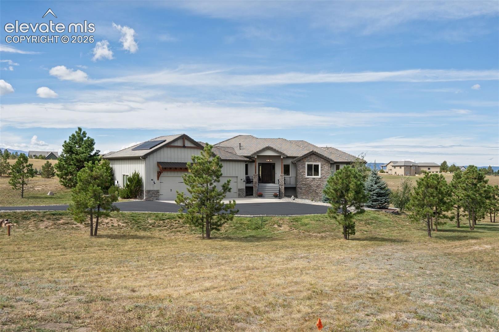 Expansive property featuring a stone and siding exterior, multi-car garage, and a wide paved driveway
