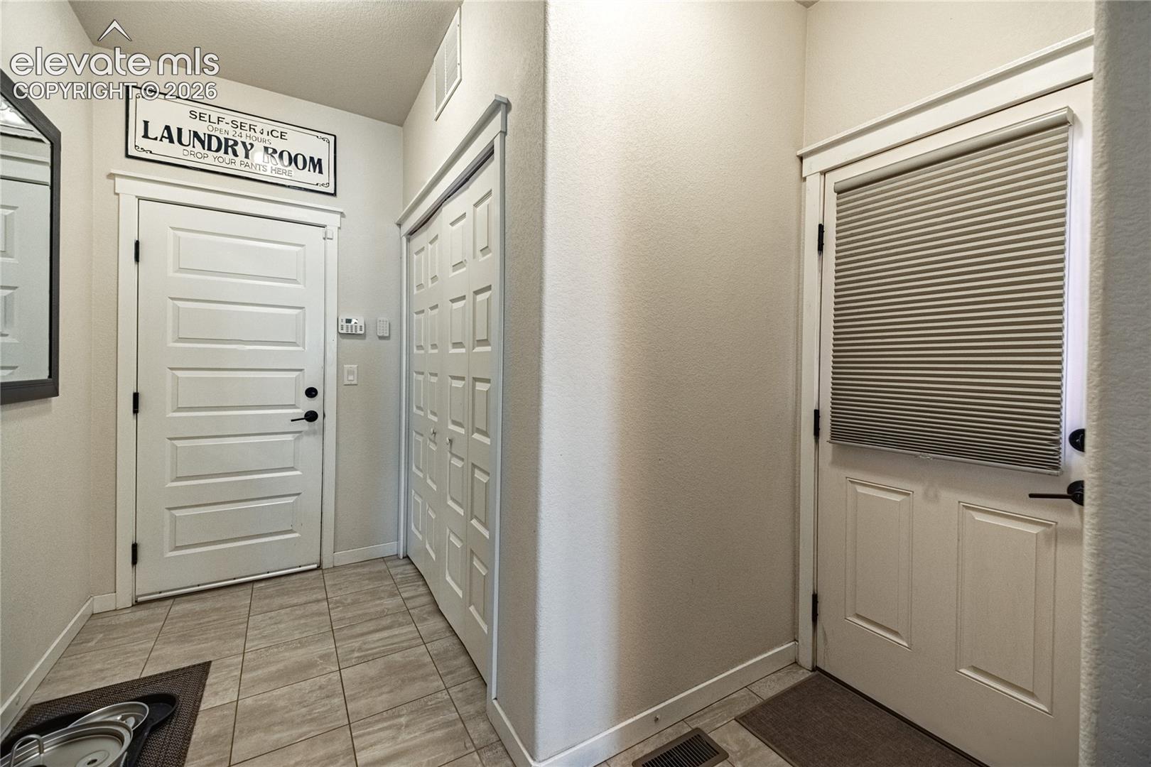 Neutral-toned tile flooring, two six-panel entry doors with matte black hardware, and double-door closet cabinetry