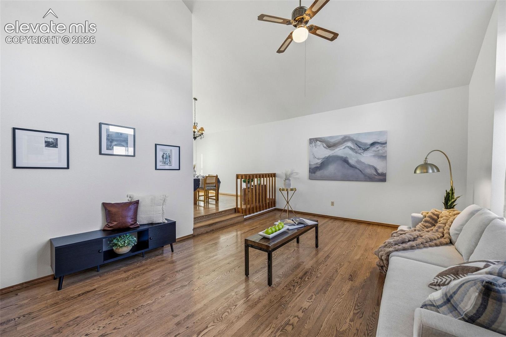 Living area featuring vaulted ceilings, wood-finish flooring, and a ceiling fan with integrated lighting