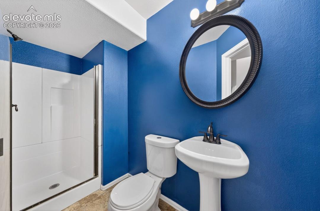Bathroom featuring a walk-in shower with a glass enclosure, pedestal sink, wall-mounted round mirror, and three-light fixture with dark hardware