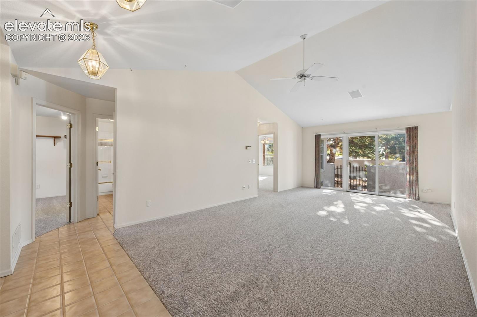 Vaulted ceiling, sliding glass doors, neutral carpeting, ceramic tile flooring, and geometric pendant lighting